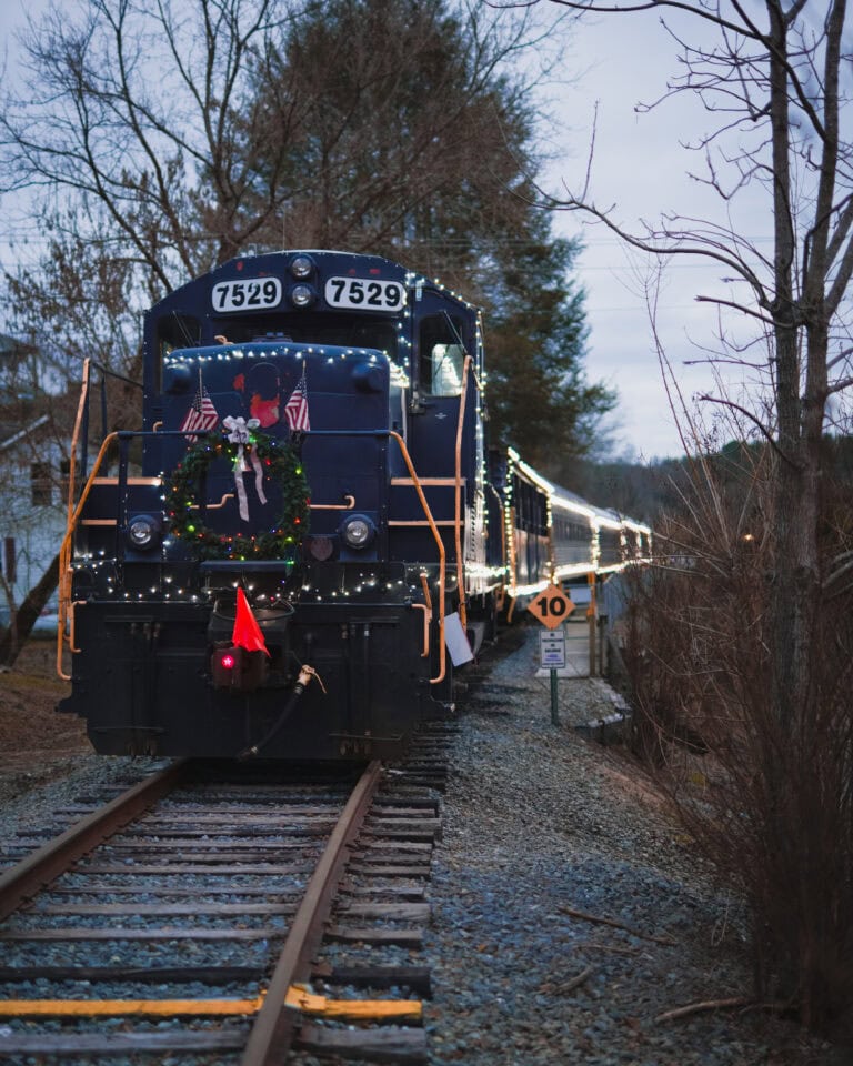 festive train decorated with Christmas lights rides through blue ridge